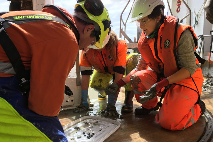 Three geologists on a boat looking at mud samples