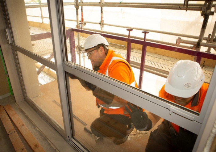 Two glaziers crouching to install a glass window at a building site  
