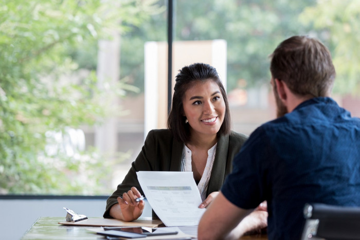 A female insurance adviser sits at a desk explaining an insurance policy to a male client