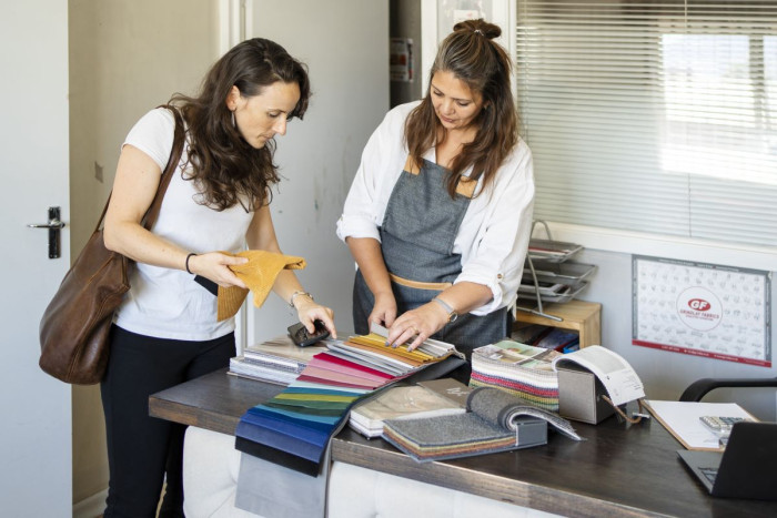 Two women stand in a display area looking at a fabric swatch 