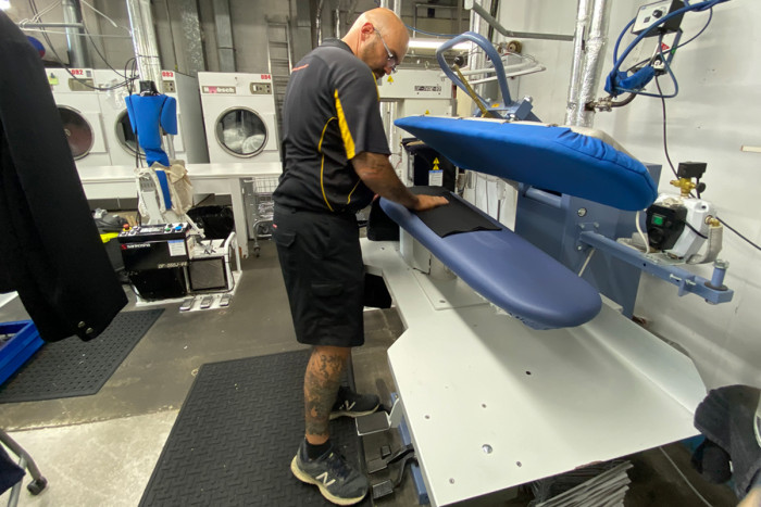 Laundry worker standing at a steam press, pressing a garment