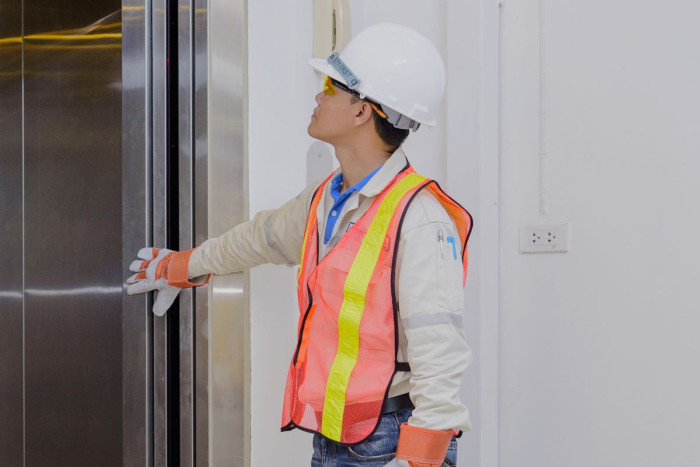 A man in a high viz vest, helmet and protective gloves stands looking into a lift 