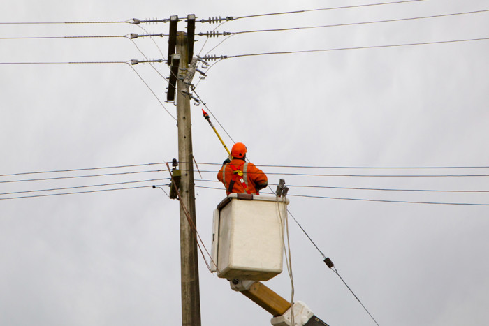 A line mechanic on a hydraulic crane disconnects power lines for repairs