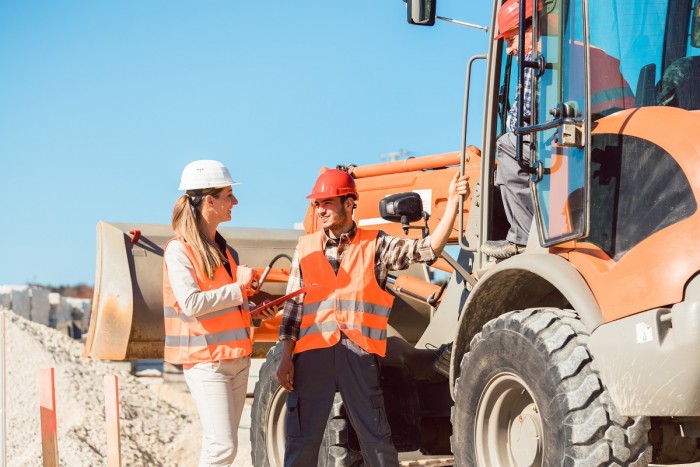 A quarry manager in a mine does a safety check on quarry machinery while chatting with two quarry workers