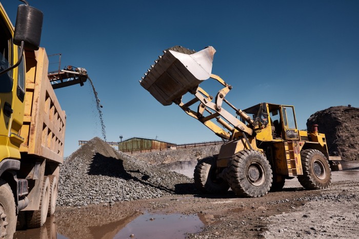 A crushing machine crushes rocks in a quarry while a man driving a loader lifts up the crushed rocks with the shovel of the loader.