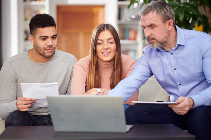 An older male mortgage broker discusses home loan options with a young couple