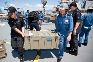 Two navy soldiers carry a big box of weapons off a navy frigate