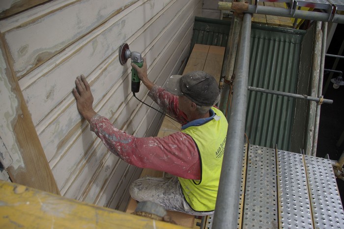 A painter and decorator sands the outside of a building to prepare it for painting