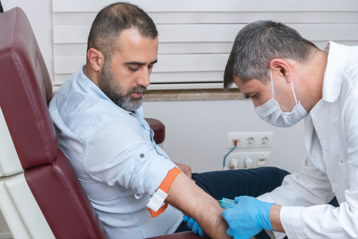 A phlebotomist draws blood from a patient sitting on a chair