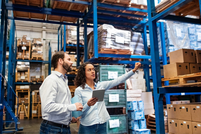 Purchasing/supply officer with a supplier, holding an ipad and pointing at goods in a warehouse