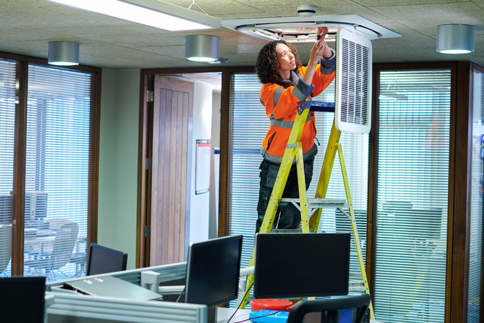 A female air-conditioning technician inspecting an air-conditioning unit in an office