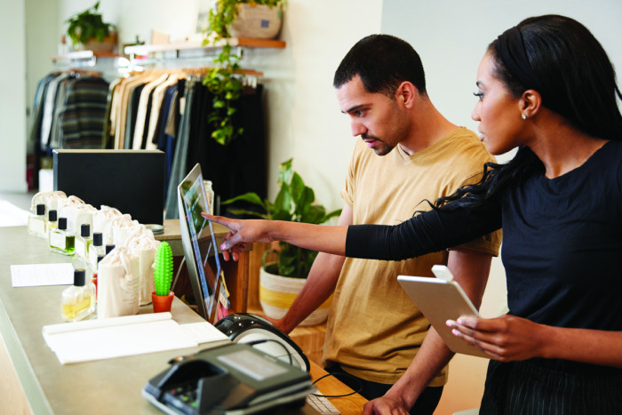 A female retail manager points out information on a computer screen to a male staff member