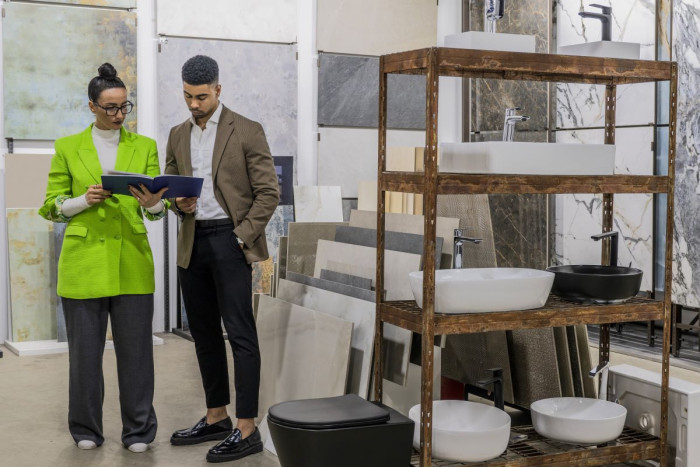 A woman in a bright jacket shows a folder to a man in a suit,  in a ceramics display area