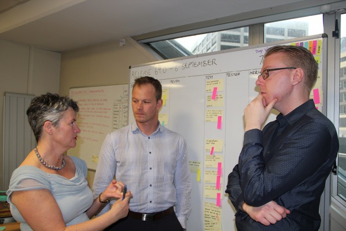 Two men and a woman standing in front of a whiteboard talking