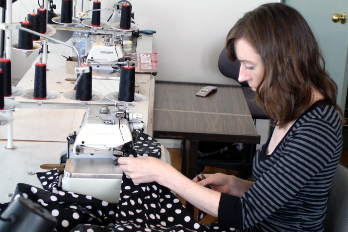 Angela Flynn guiding black material with white spots through a sewing machine