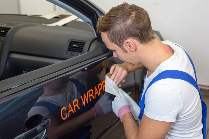 A signmaker applies a logo vinyl decal onto a car