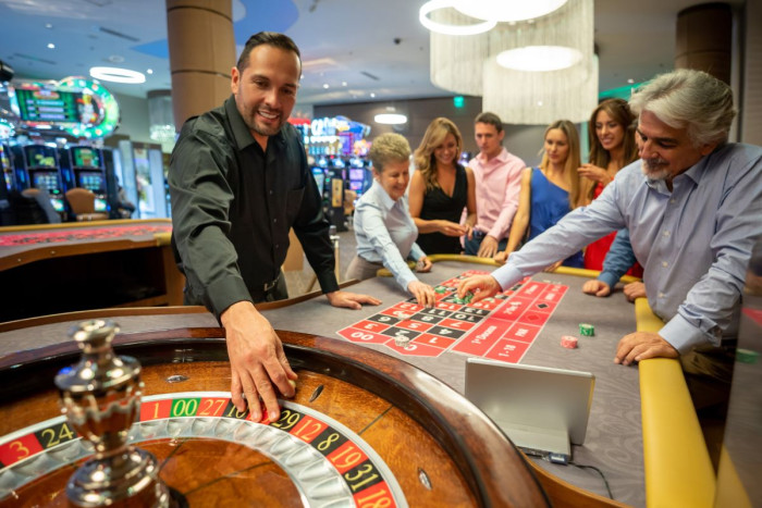 A table games dealer and gamblers stand around a roulette wheel in a casino