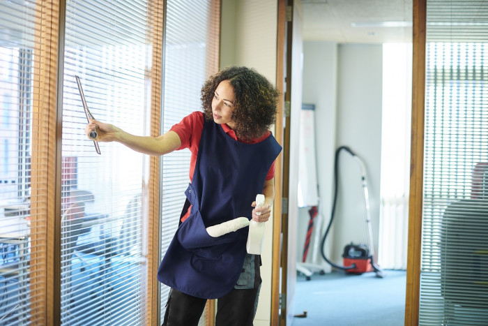 A woman uses a blade to clean soap off a window in an office