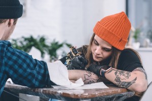 A tattoo artist draws a design on a man's arm while he frowns in pain.