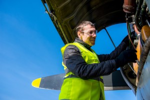 A man stands on a tiger moth airplane and inspects the engine