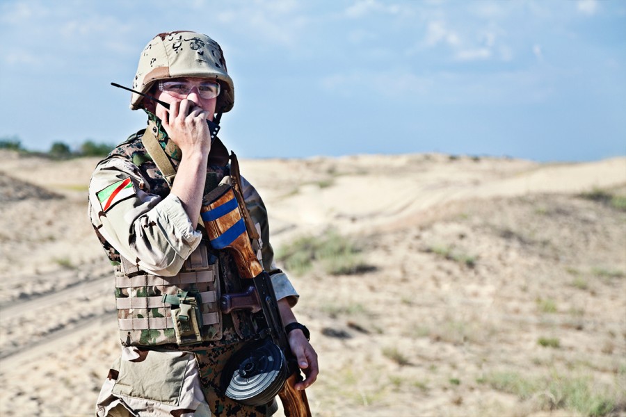 A soldier in camouflage talks into a two-way radio transceiver