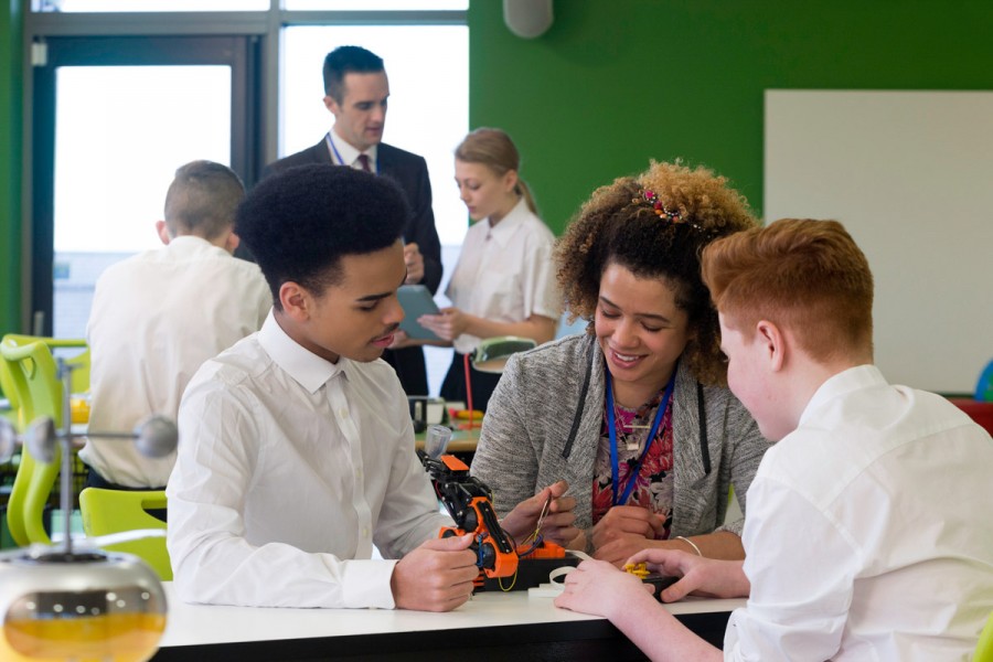 A teacher helps two students with robotics